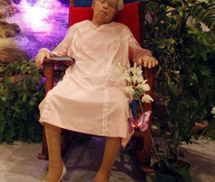 Cụ bà mặc váy cưới, ngồi ghế gỗ trong lễ tang của chính mình